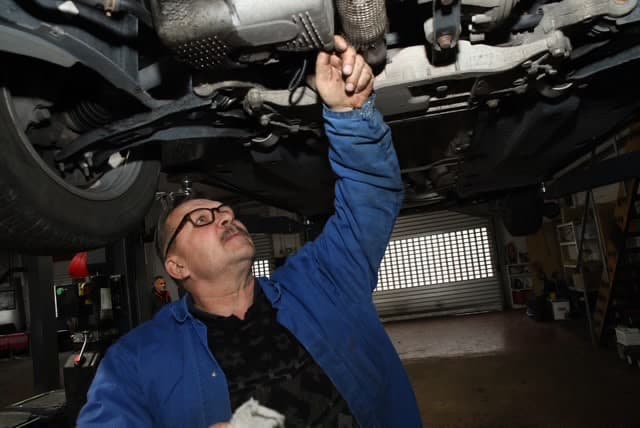 Kfz-Mechaniker arbeitet unter einem Fahrzeug auf der Hebebühne